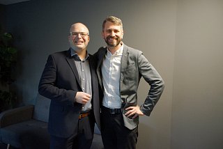 Zwei Männer in Anzügen lächeln in die Kamera