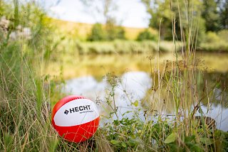 Rot-weißer Ball mit Firmenlogo liegt am Ufer eines Sees