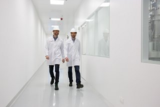 Zwei Männer in Schutzkleidung gehen lächelnd einen Flur entlang