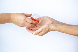 Hände überreichen sich eine Glaskugel mit orangenem Inhalt